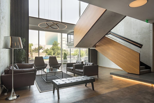 A modern lobby with leather sofas, a glass coffee table, and a staircase with a wooden finish. - Sheraton Novi Sad (Novi Sad)