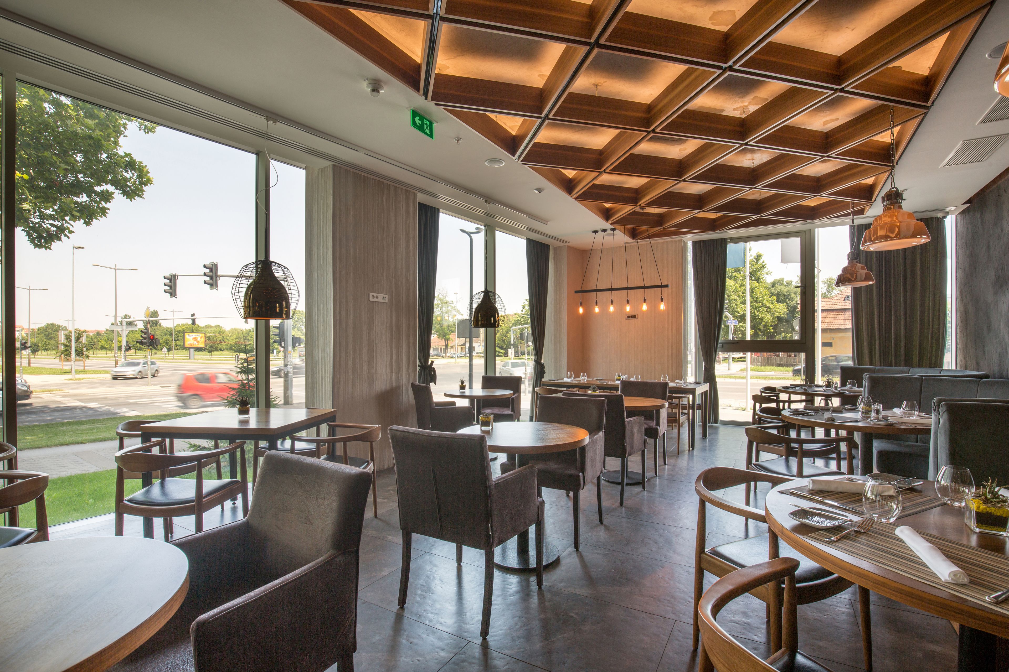 A restaurant with a modern interior, featuring a grid-patterned ceiling, large windows, and a variety of seating arrangements including tables and chairs.