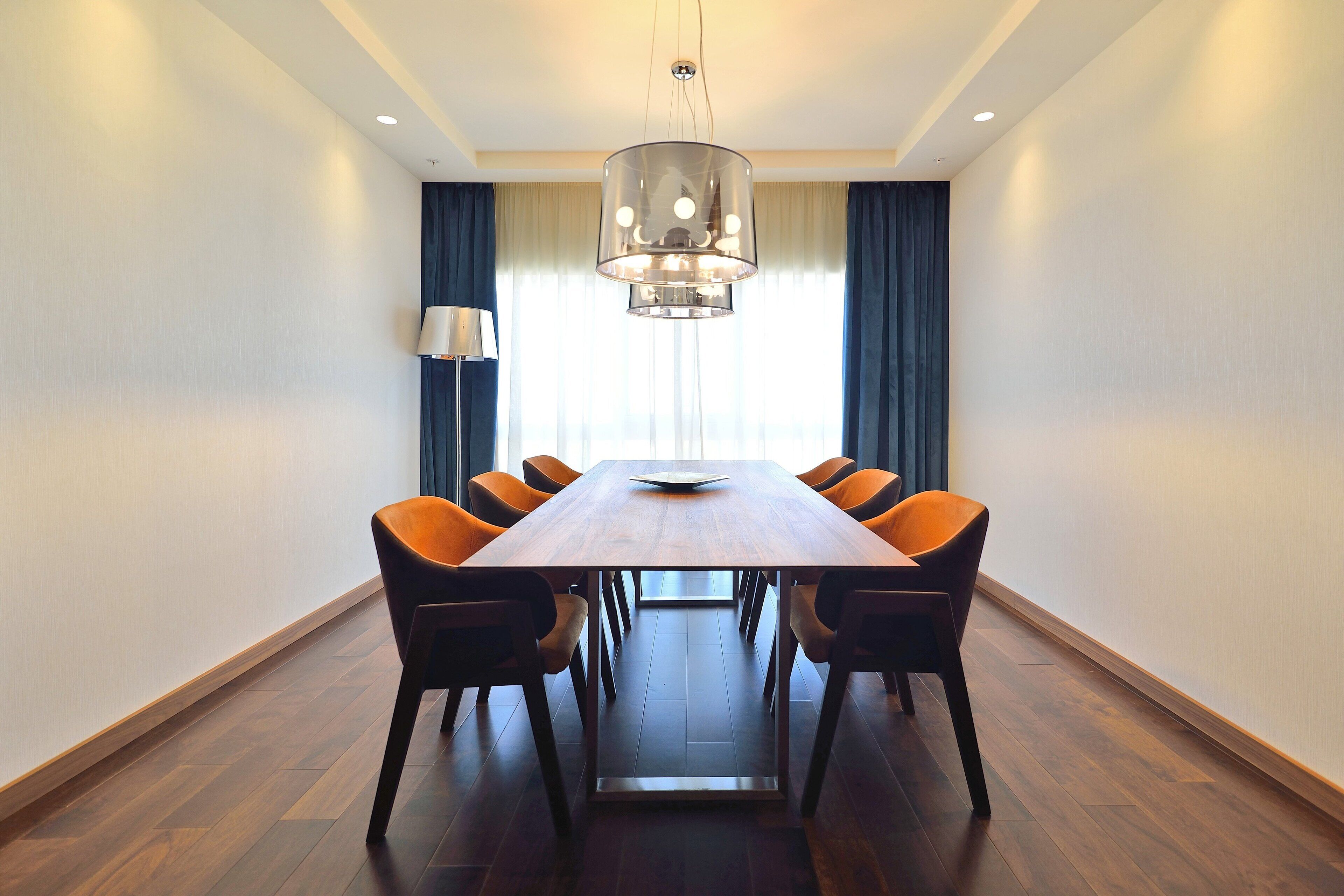 Une salle de conférence avec une table en bois, six chaises, un lustre moderne et un lampadaire.