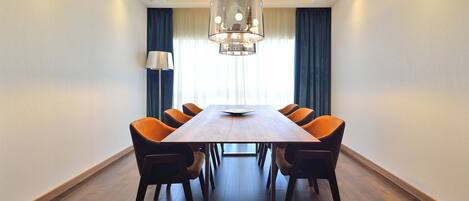 Un salón de conferencias con una mesa de madera, seis sillas, una lámpara de araña moderna y una lámpara de pie.