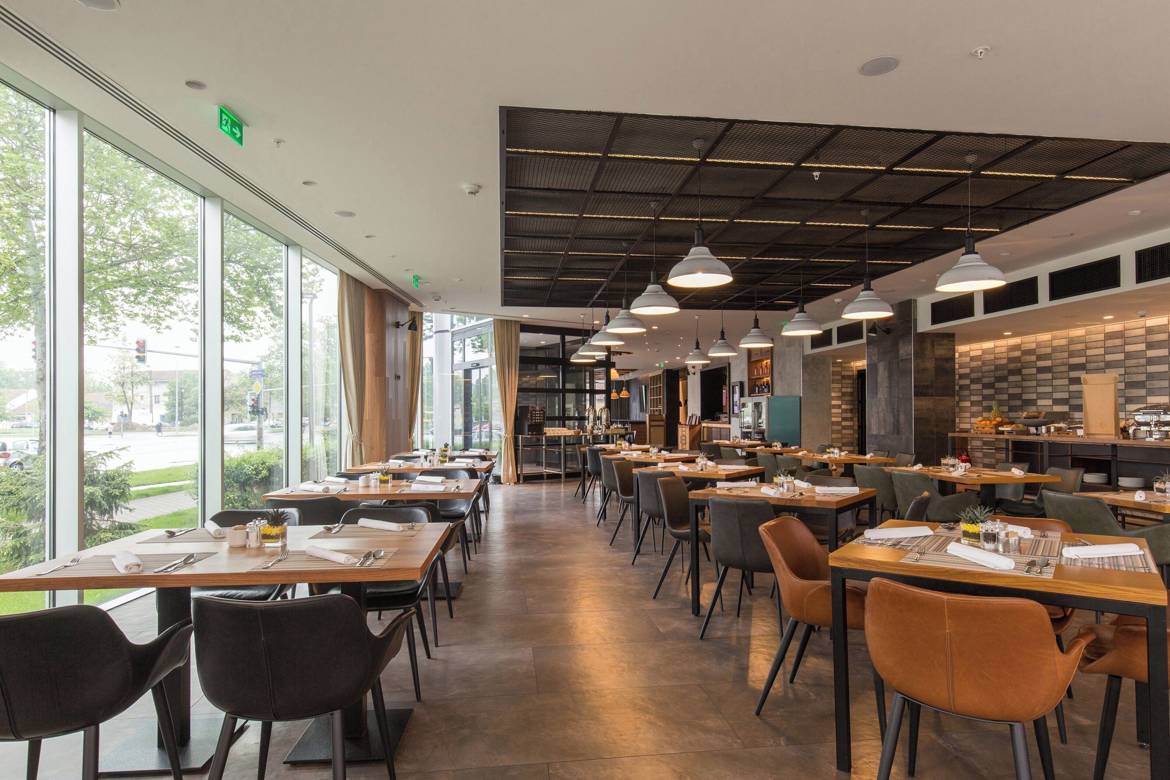 A modern restaurant with long tables, chairs, and pendant lighting.