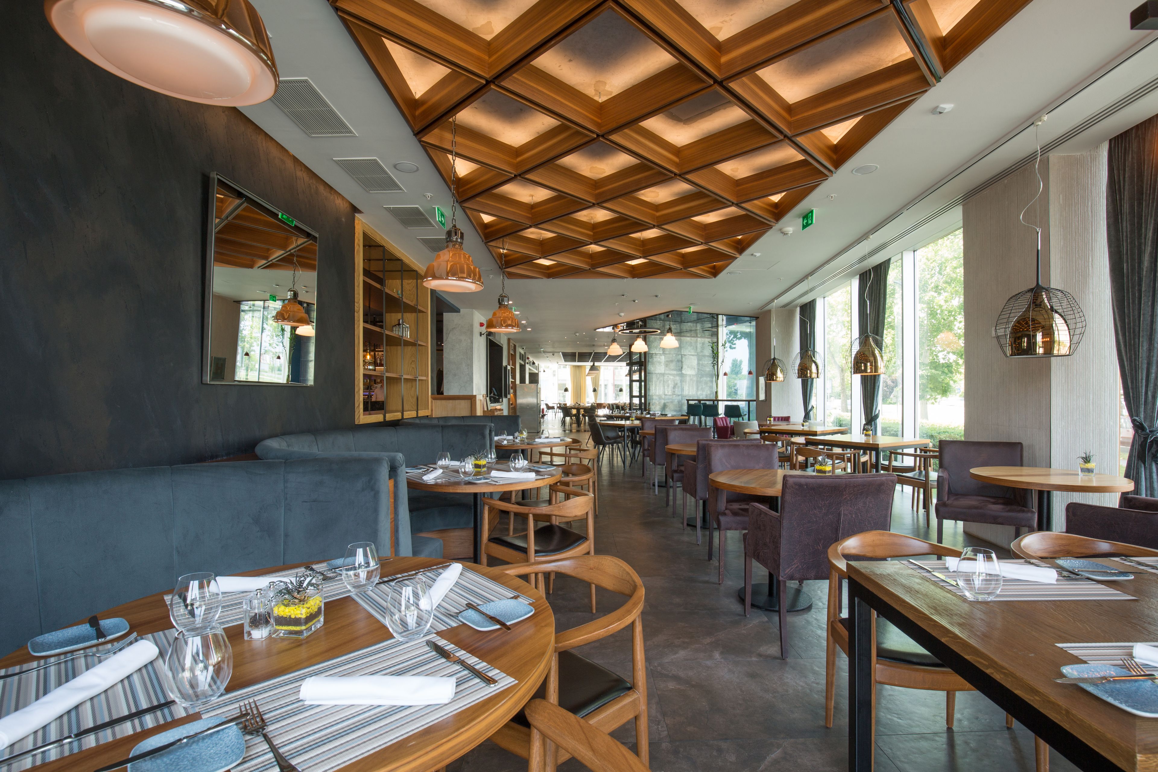 A modern restaurant interior with wooden tables, cushioned seating, and pendant lighting.