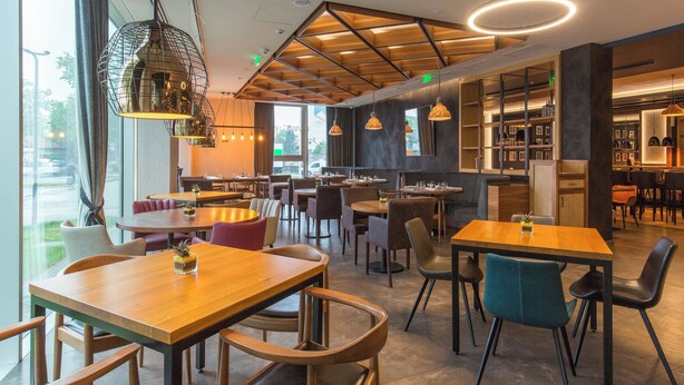 A modern restaurant with wooden tables and chairs, pendant lighting, and a view of the outdoors. - Sheraton Novi Sad (Novi Sad)