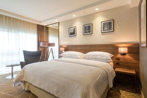 A hotel room with a large bed, a desk, a chair, and a lamp. There are three framed pictures on the wall. - Sheraton Novi Sad (Novi Sad)