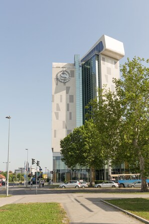 A modern building with a prominent clock on the facade, surrounded by a well-maintained grassy area and a few parked cars. - Sheraton Novi Sad (Novi Sad)