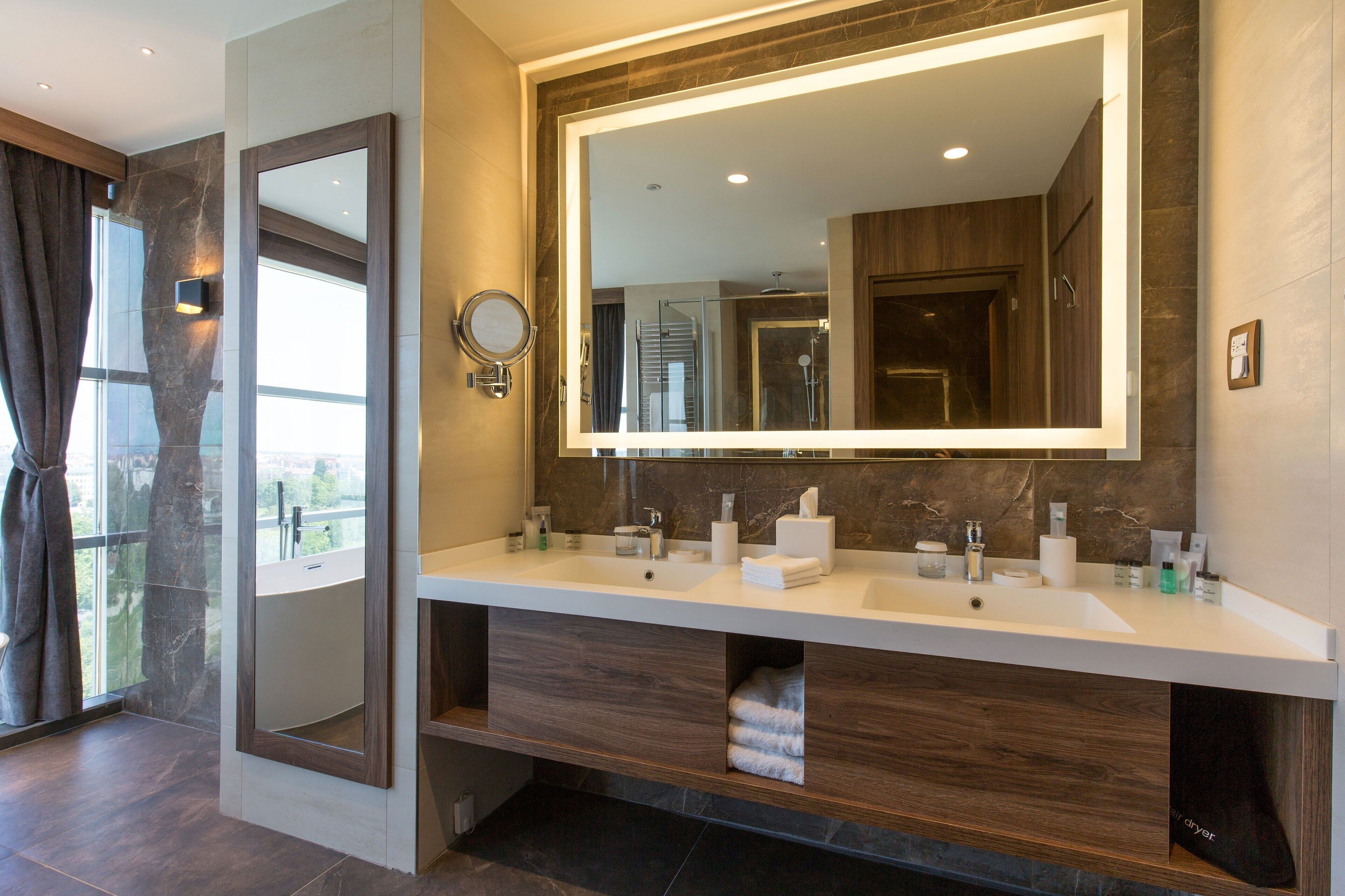 A modern bathroom with a large mirror, dual sinks, and a built-in shower.