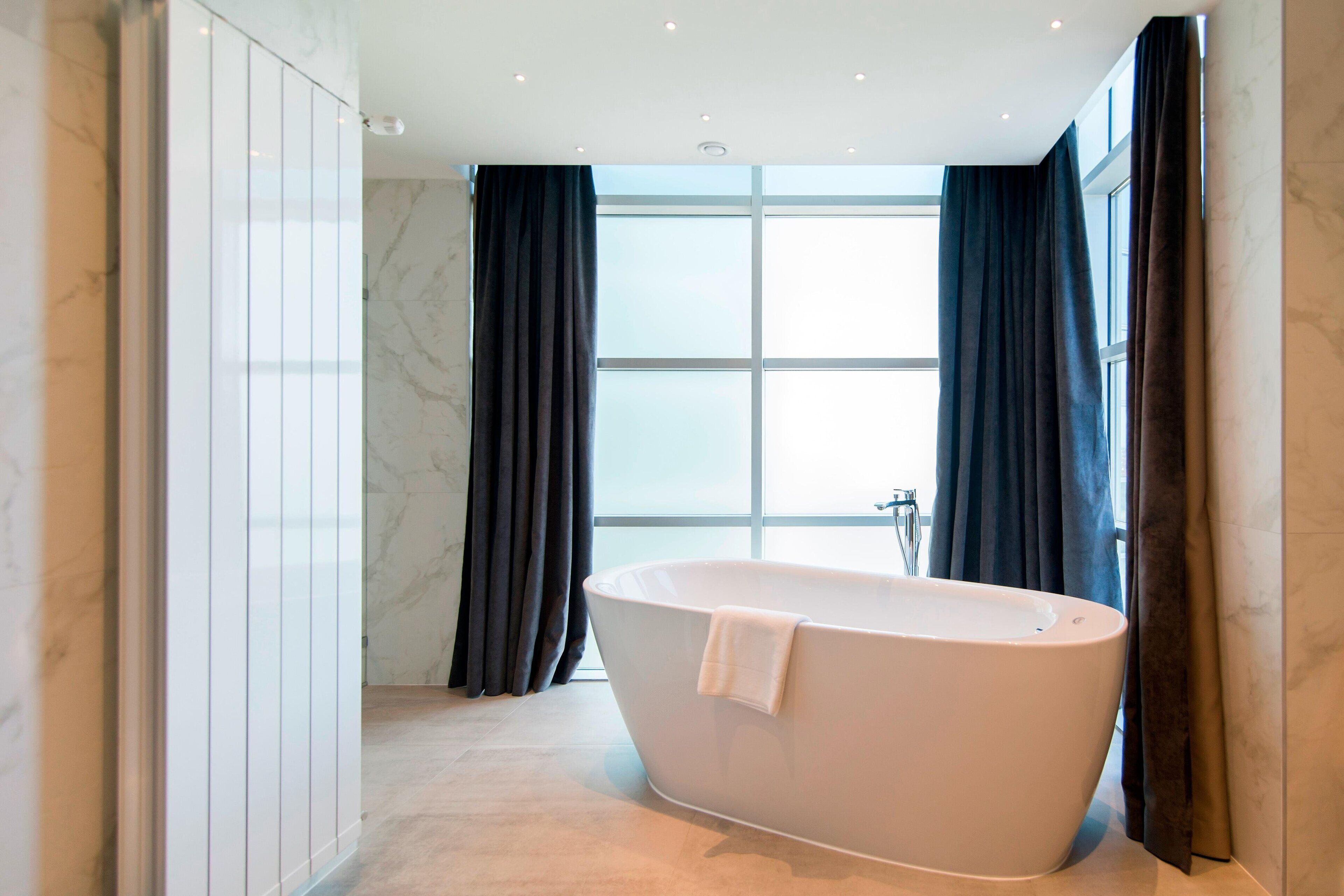 Een moderne badkamer met een vrijstaand bad, grote ramen en marmeren wanden.