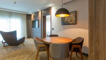 Una habitación de hotel moderna con una mesa de comedor redonda de madera, cuatro sillas grises, una lámpara colgante negra y un cuadro abstracto grande en la pared.