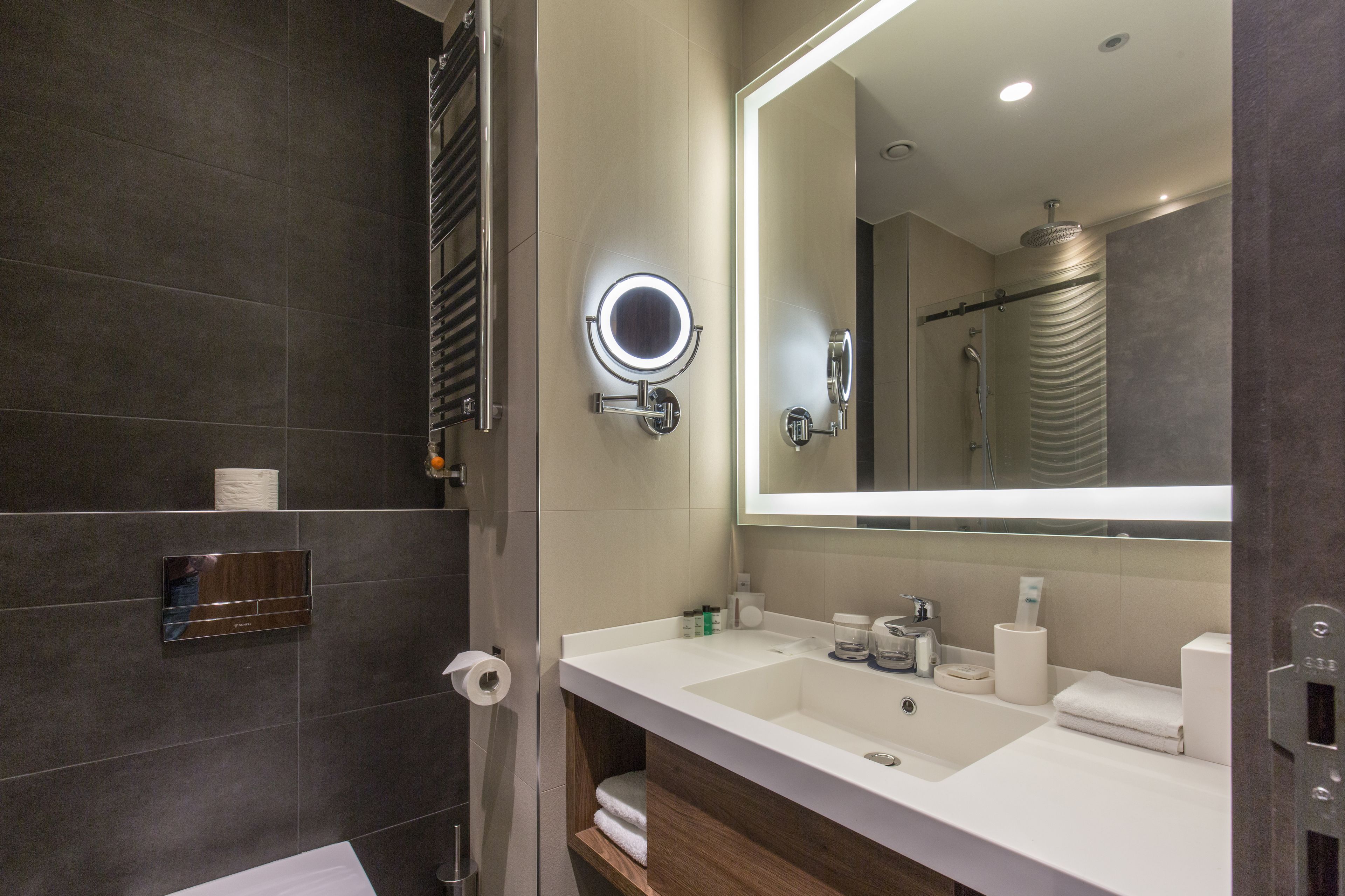 A modern bathroom with a large mirror, two sinks, and a shower.