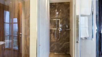 A modern bathroom with a glass shower enclosure, marble walls, and a glass door.