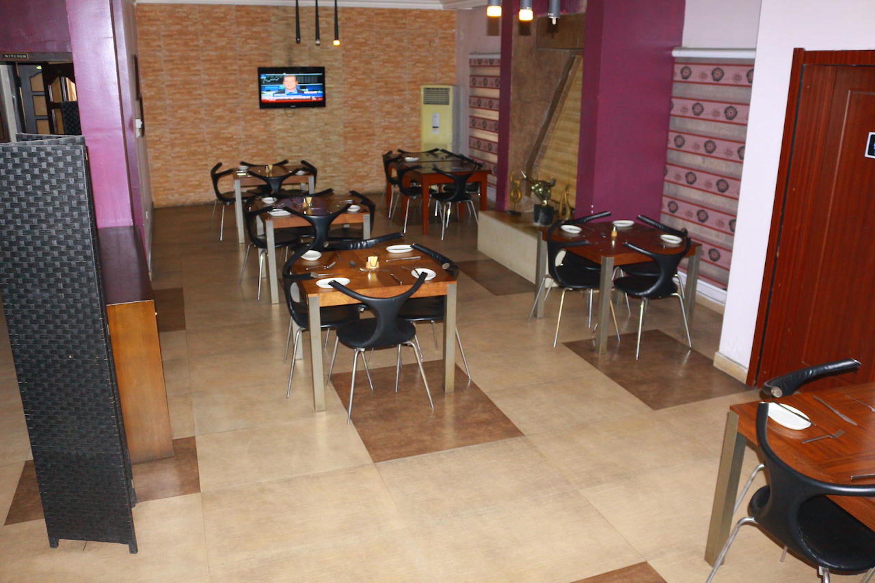 A restaurant with multiple tables and chairs, a television mounted on the wall, and a staircase in the background.