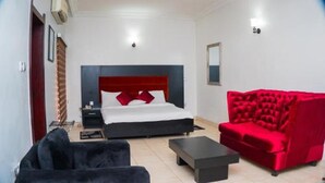 Una habitación de hotel con una cama, un sillón rojo, un sofá negro y una mesita.