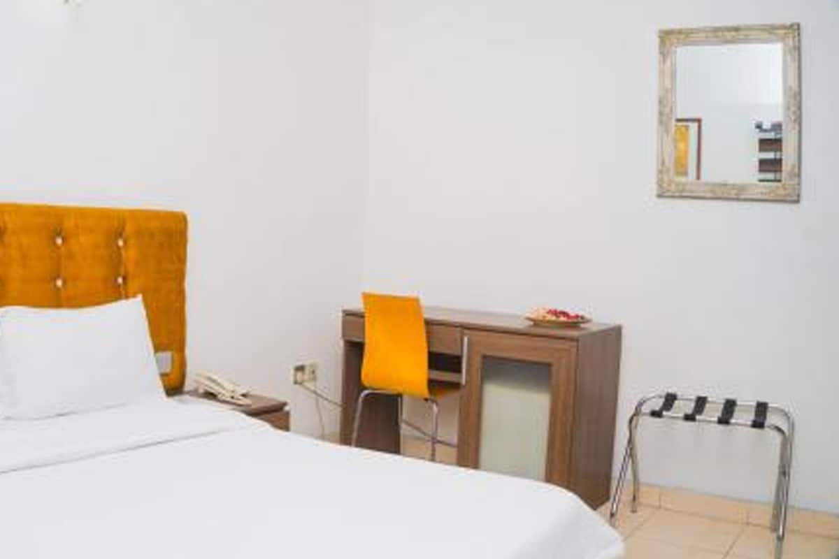 Een hotelkamer met een bed, een bureau, een stoel, een klein tafeltje en een spiegel aan de muur.