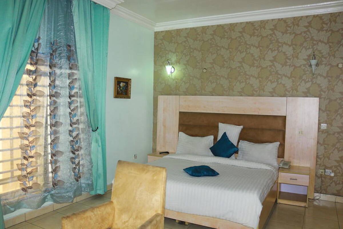 Een slaapkamer met een bed, nachtkastje, stoel en raam met gordijnen.
