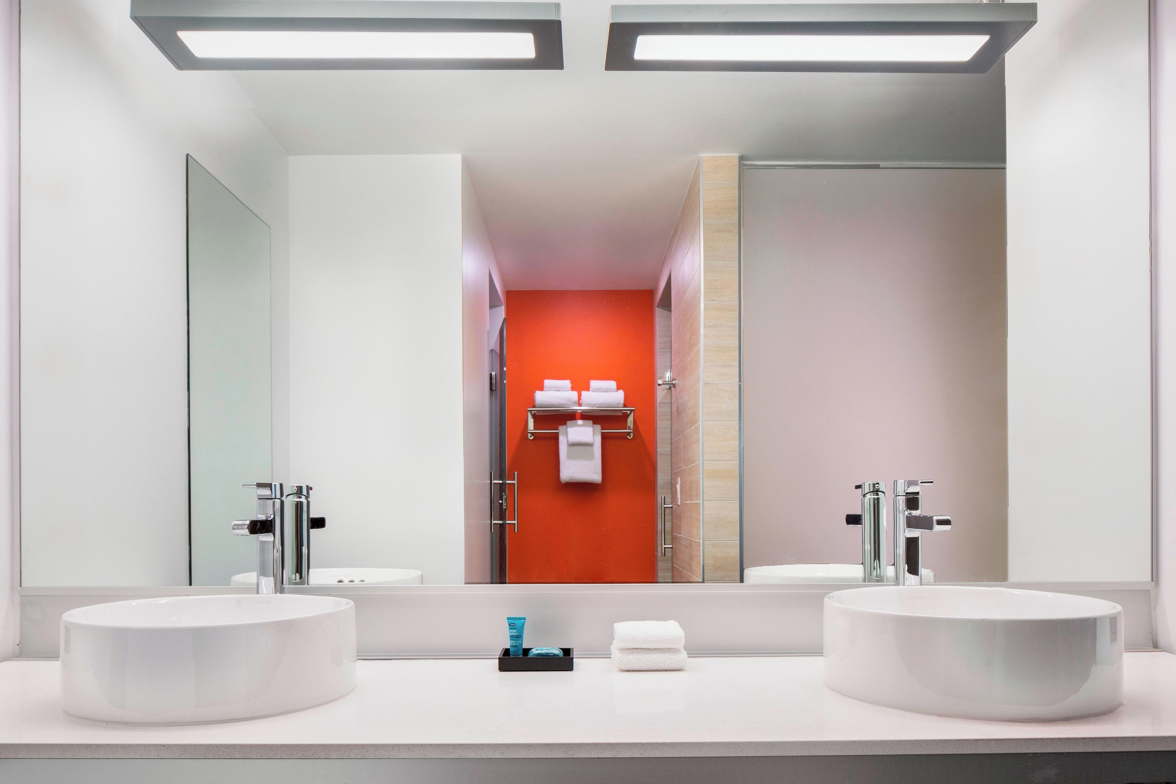 A modern bathroom with two sinks, a large mirror, and a red accent wall.