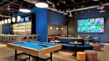 Une table de billard avec des billes, un bar avec des étagères remplies de bouteilles et un espace détente avec des tables et des chaises.