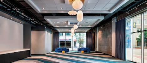 Un amplio vestíbulo de hotel con diseño moderno, que incluye una larga recepción, ventanas grandes y una alfombra estampada.