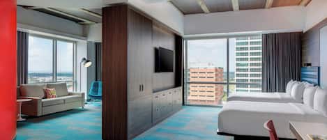 A modern hotel room with a large bed, a sofa, a TV, and a view of the cityscape.