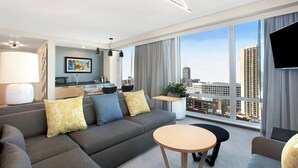 A modern hotel room with a grey sofa, a round wooden table, and a city view through large windows. - Courtyard by Marriott Boston Downtown/North Station (Boston)