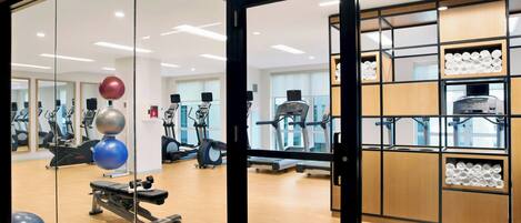 A gym with exercise equipment, a mirrored wall, and wooden cabinets with exercise balls.