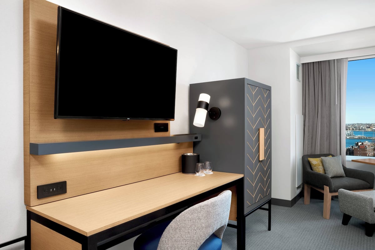 Een moderne hotelkamer met een flatscreen televisie, een houten bureau, een stoel, een sofa en uitzicht op de stad.