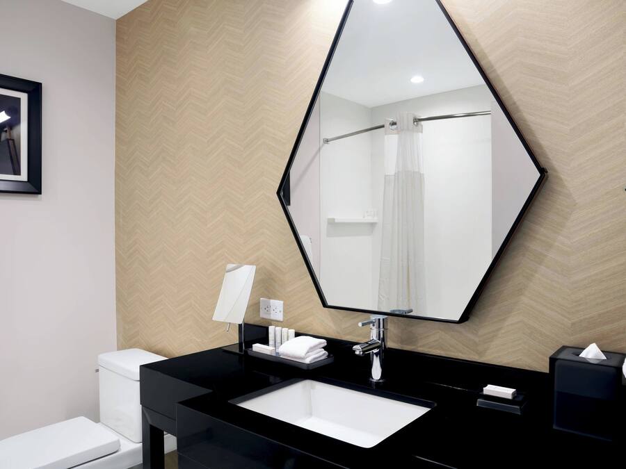 Un baño moderno con un lavamanos negro, un espejo grande y un inodoro blanco.