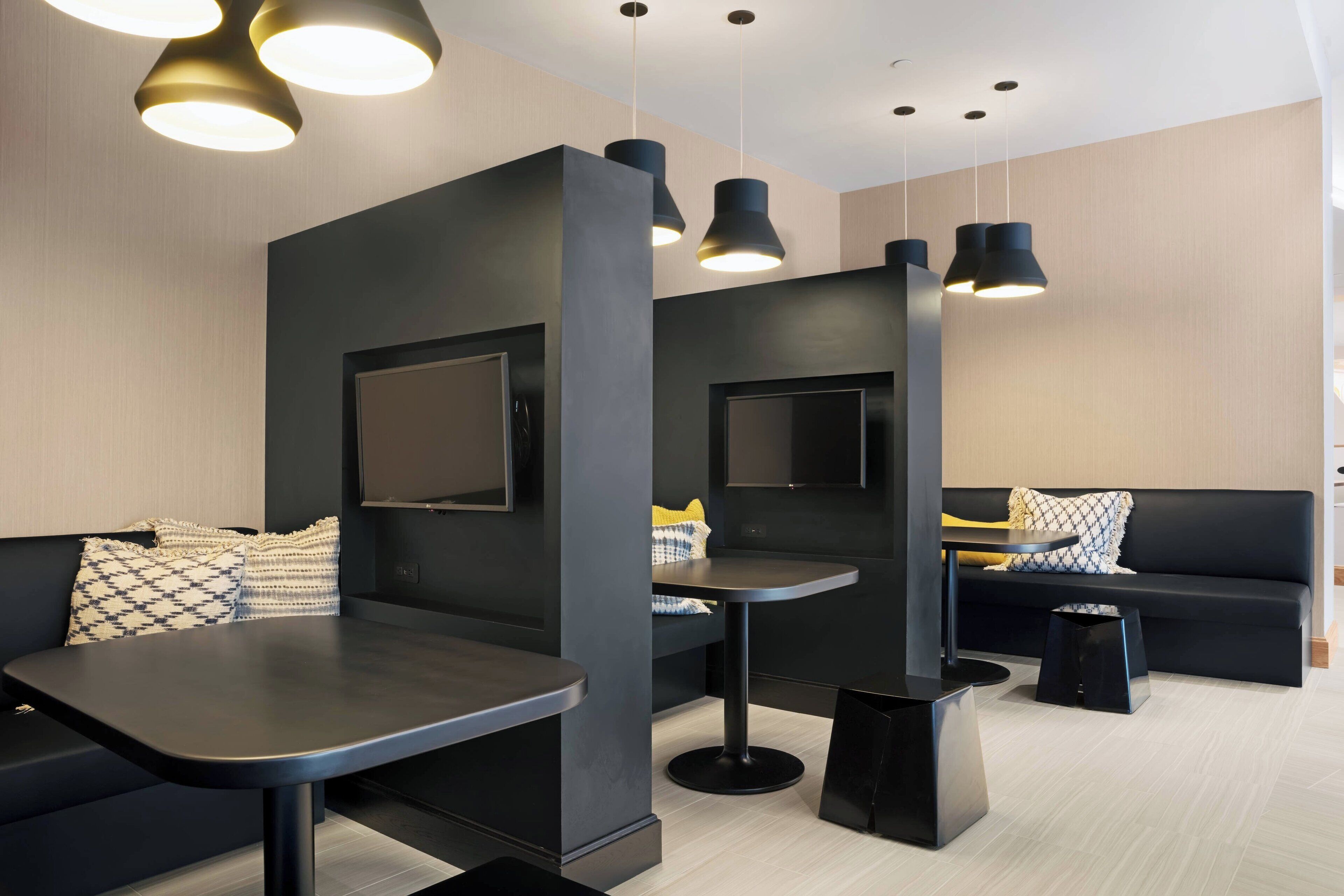 Eine moderne Lounge mit schwarzen Sofas, einem runden Tisch und Pendelleuchten.