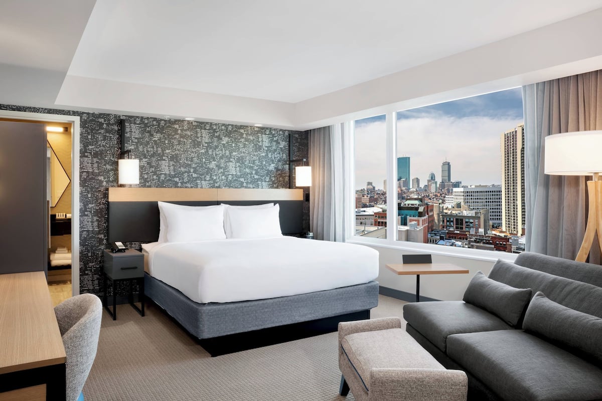 Een moderne hotelkamer met een groot bed, een sofa, een bureau en uitzicht op de stad.
