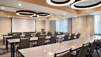 Una sala de conferencias con una mesa larga, sillas, una pantalla de proyector y un amplio ventanal con cortinas.