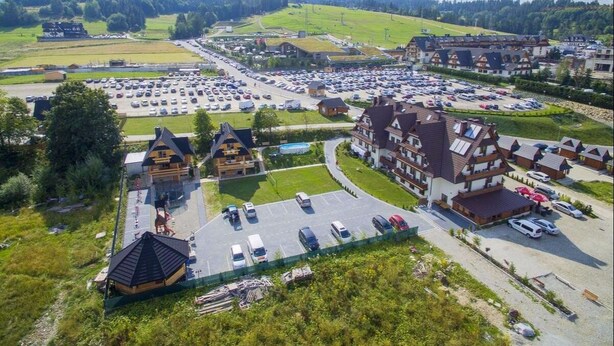 A large parking lot with multiple buildings, including a prominent lodge with a sloped roof and a swimming pool.