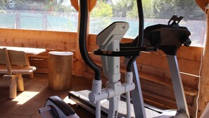 An outdoor gym area with exercise equipment, wooden benches, and a view of a garden.