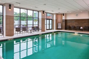 Una piscina con sillas y mesas, ventanas amplias y un reloj en la pared.