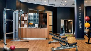 Une salle de sport équipée de matériel d’exercice, d’un miroir et d’un mur sur lequel est inscrit le texte « FITNESS STRENGTH ».