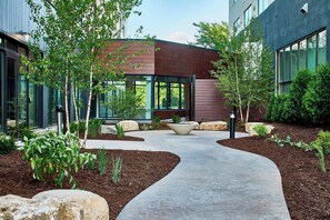 A modern building with a curved pathway, surrounded by landscaped areas with rocks and plants. - Courtyard by Marriott Minneapolis West (St. Louis Park)