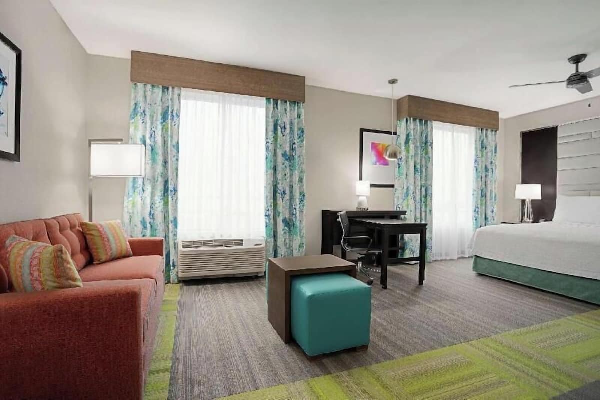 A hotel room with a bed, a desk, a chair, a sofa, and a small ottoman.
