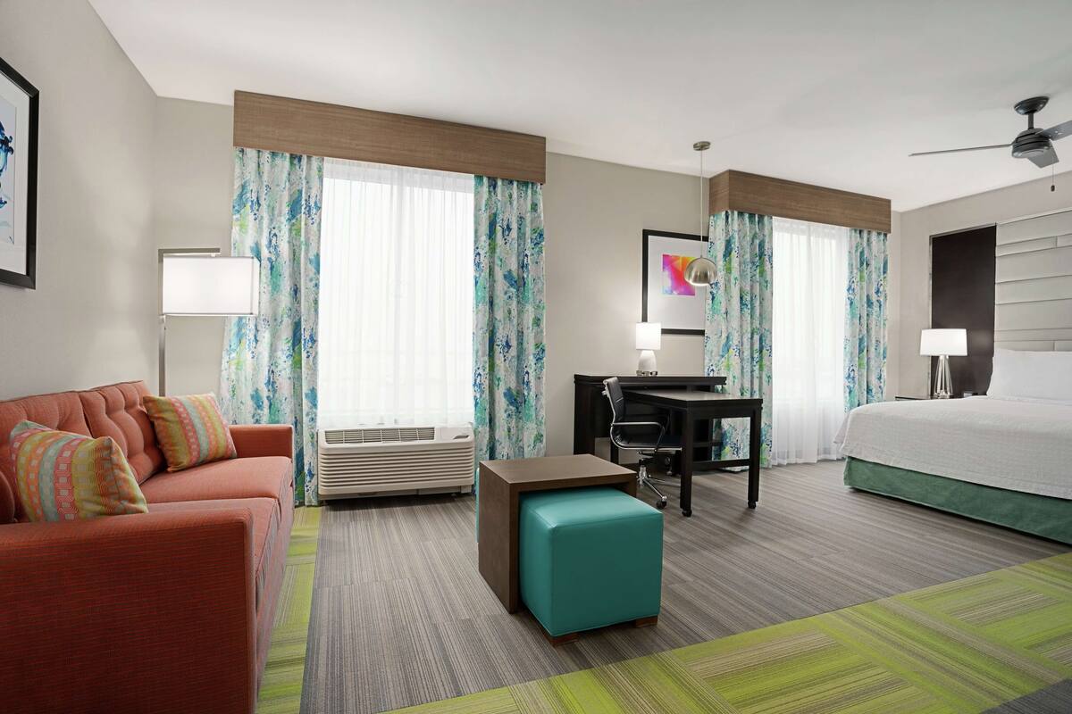 A hotel room with a bed, a desk, a sofa, and a small ottoman.
