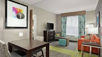 A hotel room with a dining table, sofa, TV, and a framed picture on the wall.