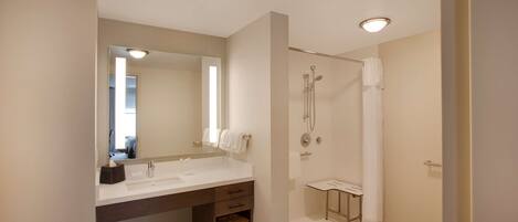 A modern bathroom with a large mirror, dual sinks, a shower, and a vanity with storage.