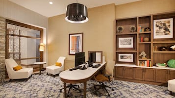 A modern office space with a desk, two chairs, a computer setup, and a bookshelf with various items.