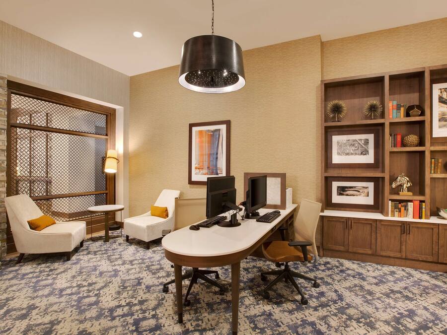 A modern office space with a desk, two chairs, a computer setup, and a bookshelf with various items.
