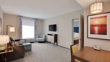 A hotel room with a sofa, armchair, flat-screen TV, and a dining table.