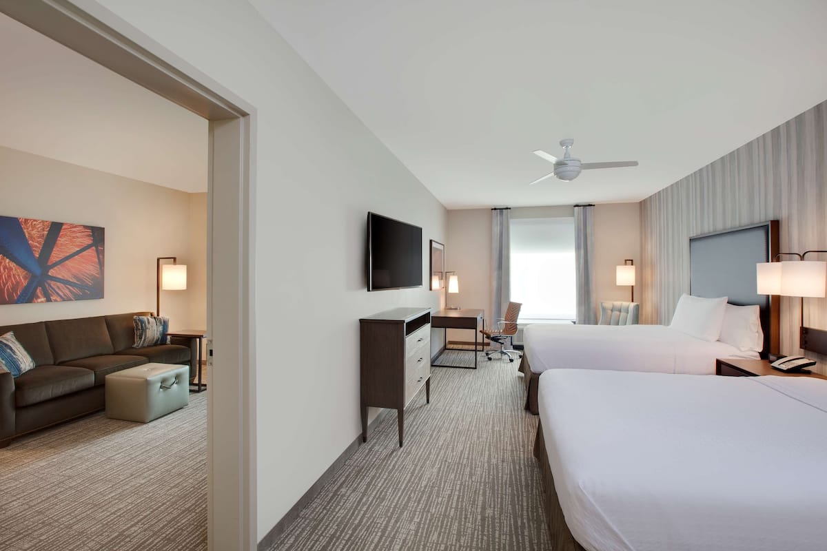 Une chambre d’hôtel avec deux lits, un bureau, une chaise, une télévision et un ventilateur de plafond.