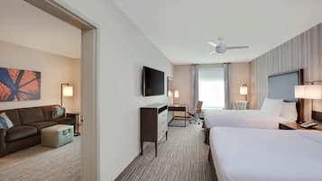 Een hotelkamer met twee bedden, een bureau, een stoel, een televisie en een plafondventilator.