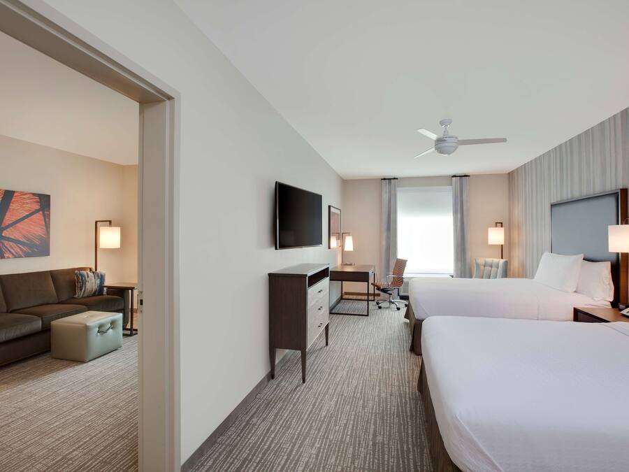 Een hotelkamer met twee bedden, een bureau, een stoel, een televisie en een plafondventilator.