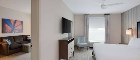 A hotel room with a bed, a TV, a desk, a chair, and a window with curtains.