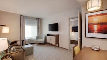 Habitación de hotel con sofá, escritorio, televisión, silla y un cuadro en la pared.