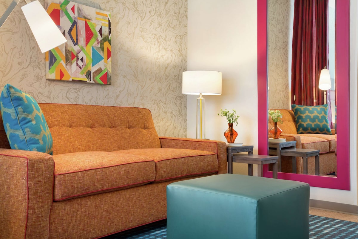 A modern living room with a sofa, ottoman, lamp, and abstract art on the wall.