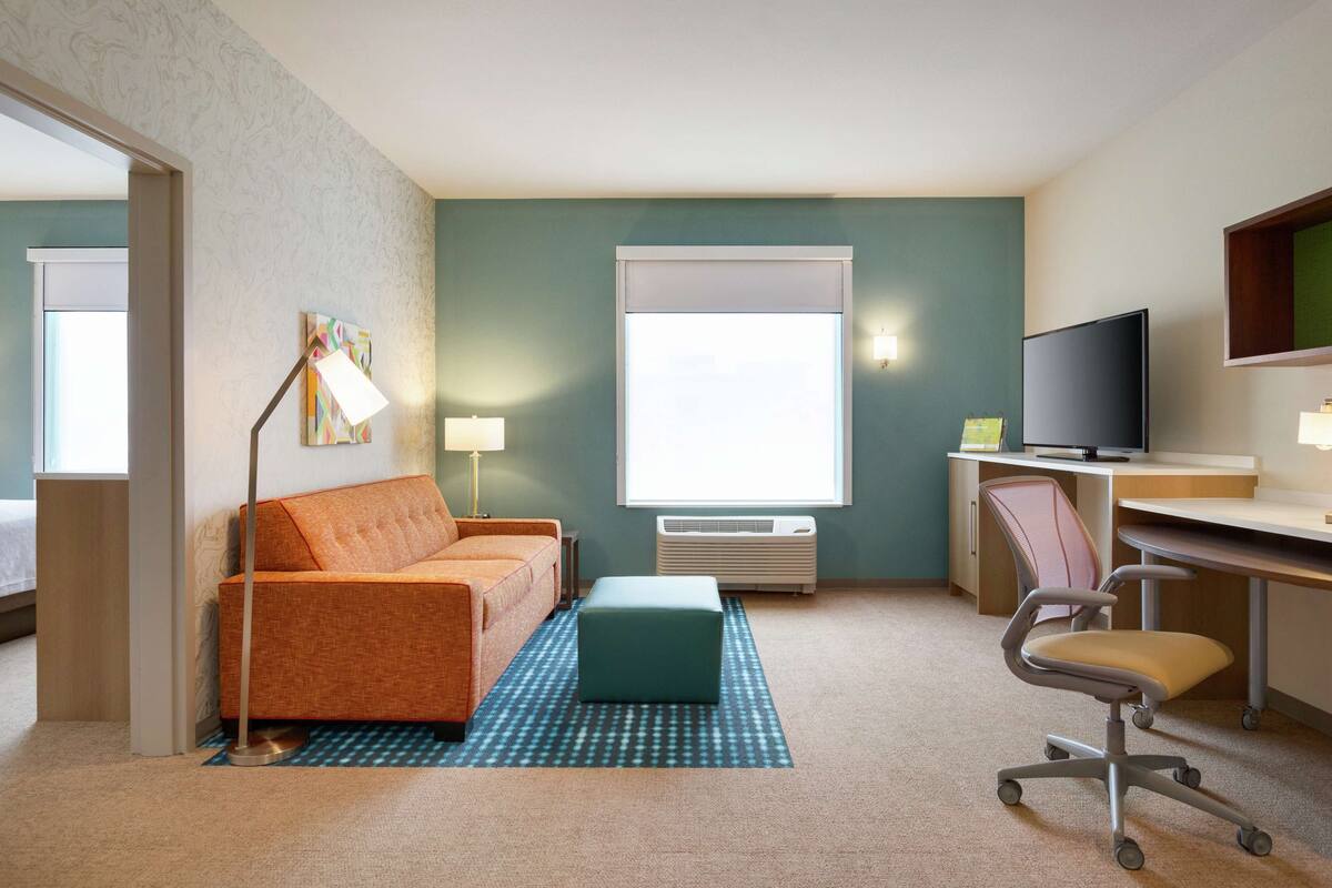 A hotel room with a sofa, a desk, a chair, a TV, and a window.