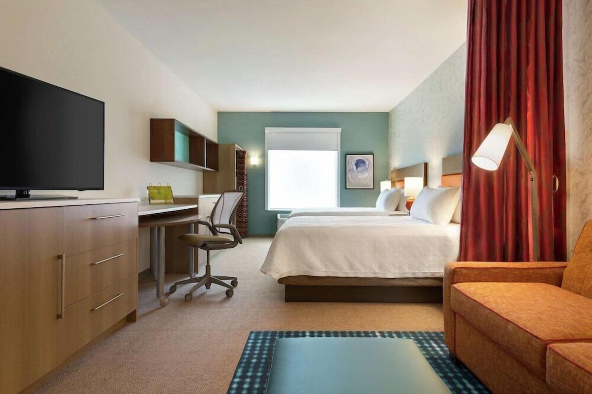 A hotel room with a bed, a desk with a chair, a television, and a window.
