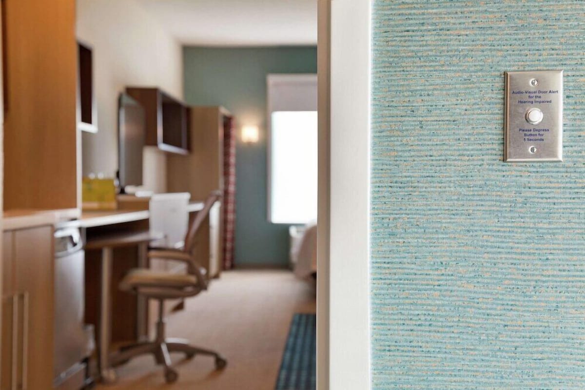 A hotel room with a kitchenette, a television, and a door with an audio-visual alert system.